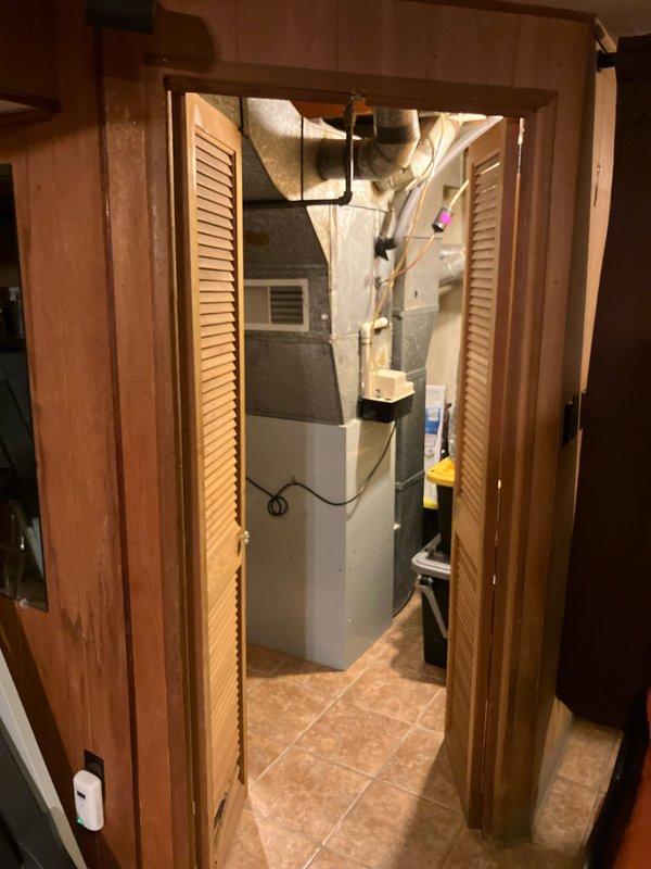 Provided estimate for replacement of a 30-year-old natural gas furnace located in basement utility closet with louvered bi-fold doors. Current unit is operational but has exceeded typical service life. Inspection revealed standard residential heating system with connected ductwork, condensate drain line, and associated mechanical components that would need to be integrated with any replacement system.
