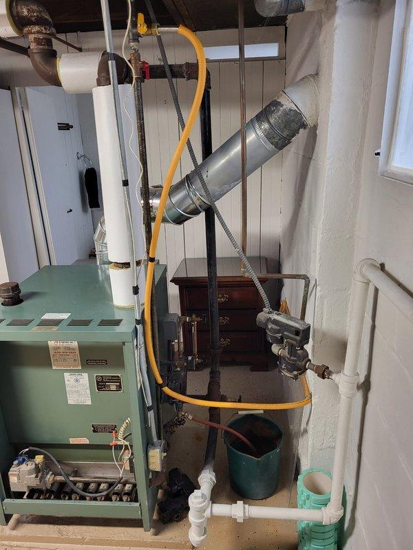 Performed assessment of 38-year-old operational steam boiler located in customer's basement. Inspection revealed aging system with visible rust on cast iron pipe sections and various connections. Documented current installation configuration including gas line, exhaust venting, and associated plumbing components for replacement estimate purposes.