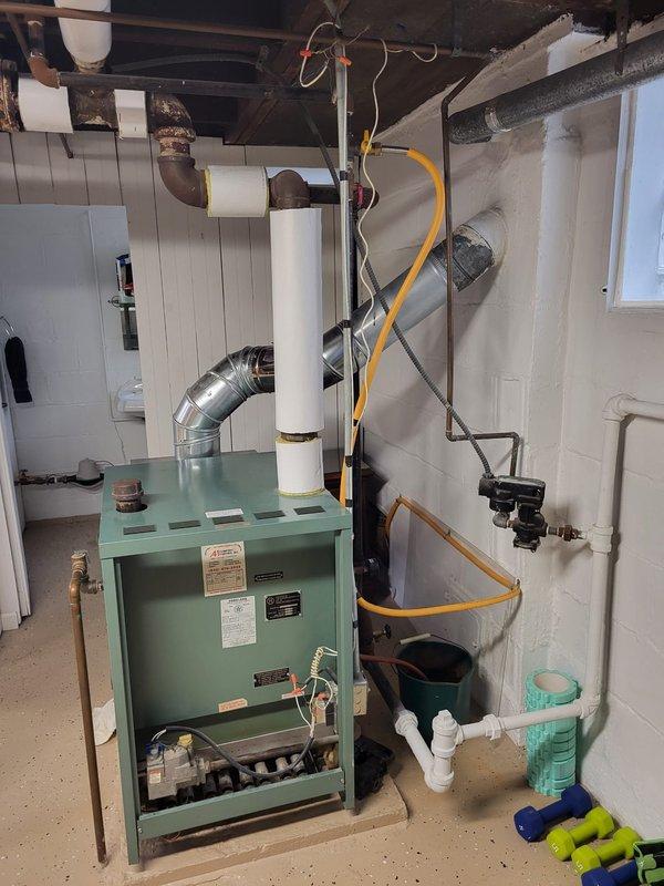 Performed assessment of 38-year-old operational steam boiler located in customer's basement. Inspection revealed aging system with visible rust on cast iron pipe sections and various connections. Documented current installation configuration including gas line, exhaust venting, and associated plumbing components for replacement estimate purposes.