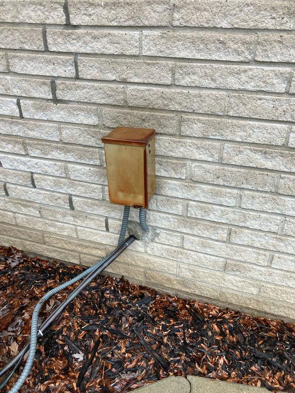 Completed assessment of non-operational A/C system over 20 years old. Observed significant weathering and oxidation on exterior electrical junction box with multiple conduits extending into ground cover. Interior inspection revealed Emerson digital thermostat (current reading 68°) mounted on interior wall with flame indicator visible. Customer seeking complete replacement of aging system.