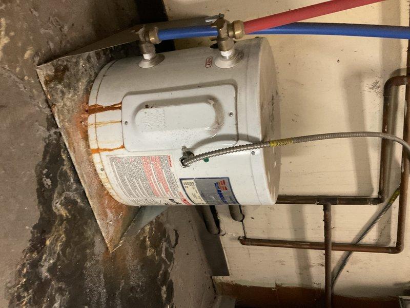Diagnosed 10-gallon commercial water heater showing active leakage from bottom of tank with visible rust/corrosion at base. Inspection revealed tank failure requiring complete replacement; documented condition with photos showing deteriorated connections and staining on surrounding concrete floor.