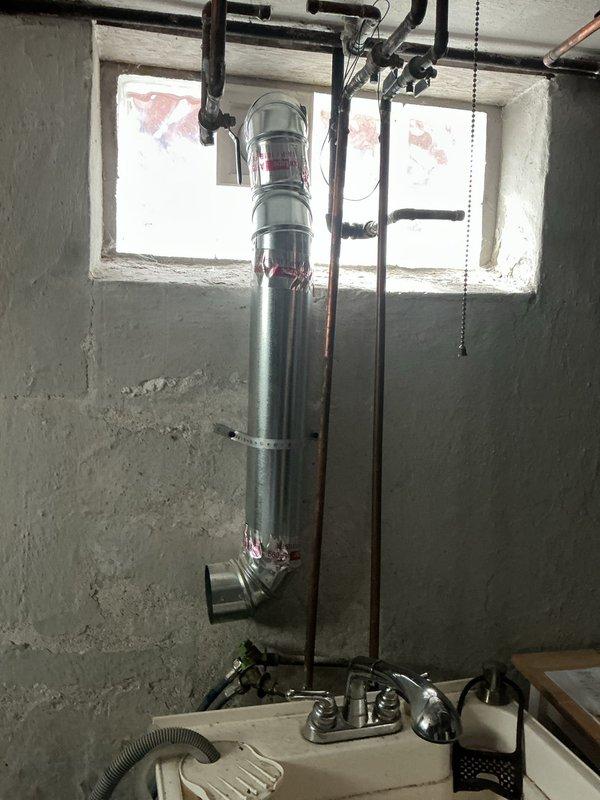 Installed new metallic dryer vent system for gas dryer in basement utility area, including vertical ductwork with properly sealed joints and a 90-degree turn at the base. Secured exhaust piping to concrete wall using appropriate metal mounting brackets, ensuring proper clearance from existing copper and black iron piping infrastructure.