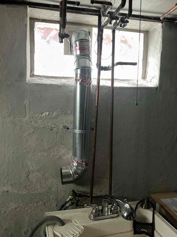 Installed new metallic dryer vent system for gas dryer in basement utility area, including vertical ductwork with properly sealed joints and a 90-degree turn at the base. Secured exhaust piping to concrete wall using appropriate metal mounting brackets, ensuring proper clearance from existing copper and black iron piping infrastructure.