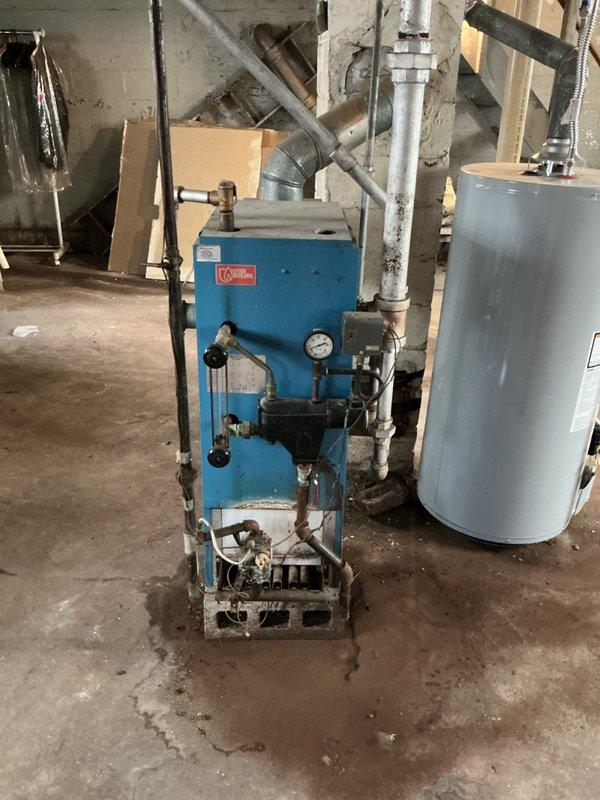 Performed inspection of 35+ year old non-functioning steam boiler with natural gas fuel source. Identified need for complete replacement of existing blue boiler unit showing significant wear and accumulation of dirt at base. Noted requirement for 4" venting installation with new boiler system to address current ventilation issues visible in concrete wall.