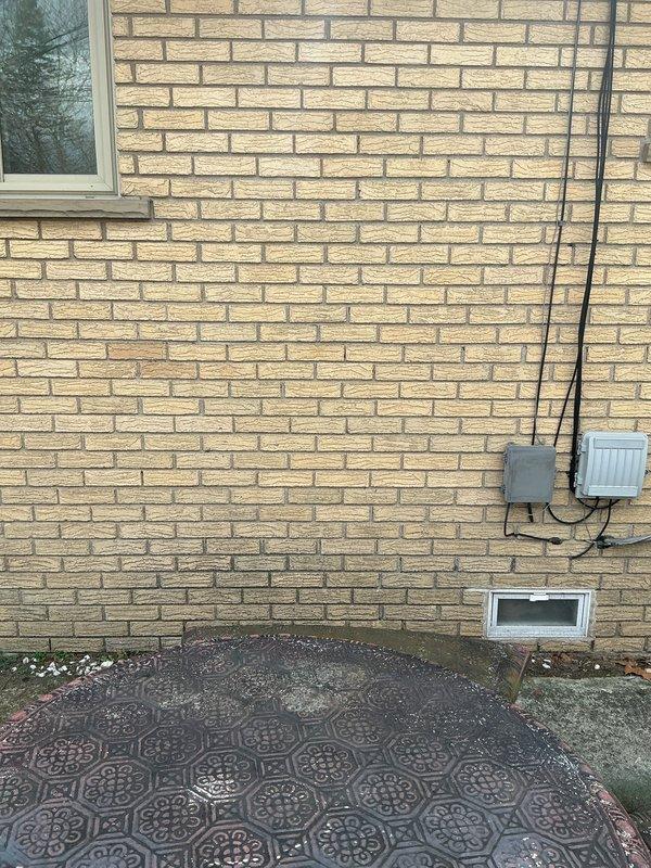 Conducted site evaluation for new mini split installation in living room and bedrooms. Assessed interior wall space for potential indoor unit placement and examined exterior brick wall with existing electrical connections for outdoor condenser unit positioning. Documented available utility access points and evaluated decorative paver area as potential location for equipment installation.