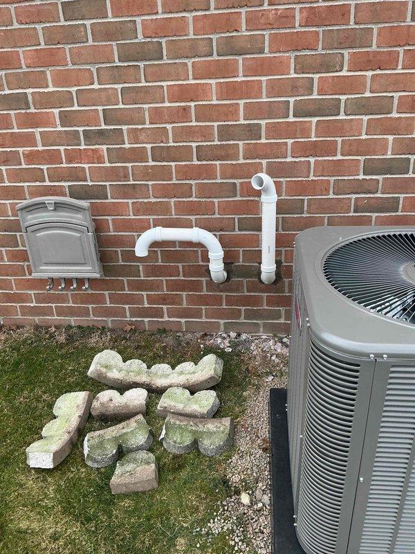Completed installation of a complete HVAC system including a 70,000 BTU furnace, 2.5-ton air conditioning unit with outdoor condenser mounted on gravel pad, and humidifier. System includes properly installed condensate pump with PVC drainage pipes secured with metal clamps, eligible for utility rebates per AHRI certification #21558665.