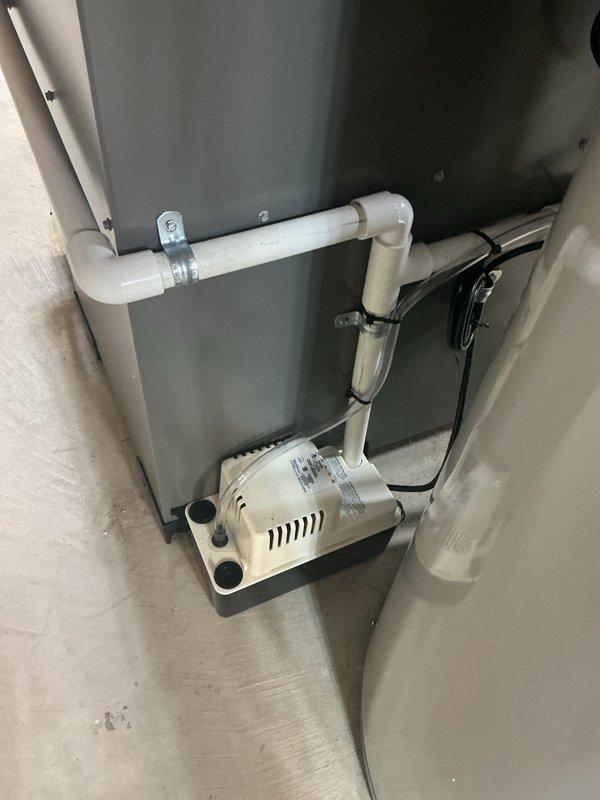 Completed installation of a complete HVAC system including a 70,000 BTU furnace, 2.5-ton air conditioning unit with outdoor condenser mounted on gravel pad, and humidifier. System includes properly installed condensate pump with PVC drainage pipes secured with metal clamps, eligible for utility rebates per AHRI certification #21558665.