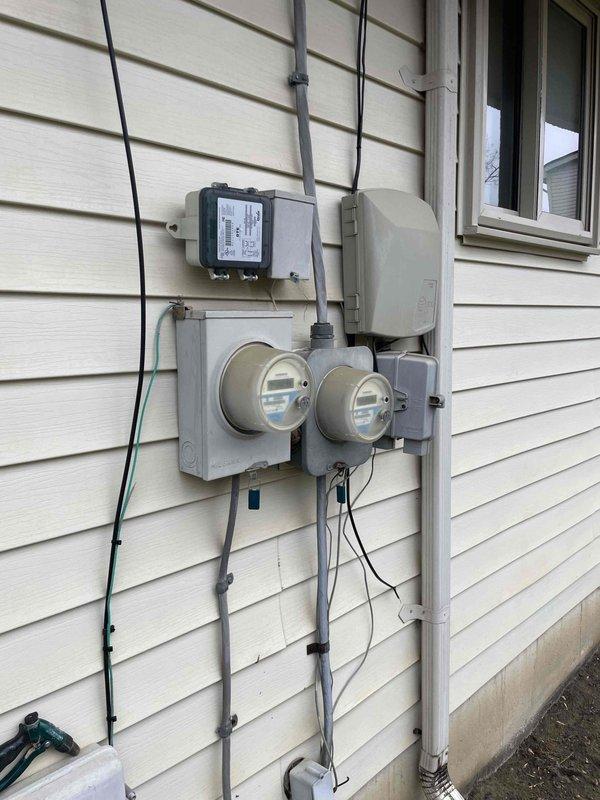 Conducted inspection of existing 10+ year old furnace and air conditioning system located in basement with natural gas fuel source. Exterior assessment revealed aging outdoor AC unit with weathering on electrical junction box and debris accumulation near foundation. Documented current electrical service configuration including dual meters and associated distribution equipment to evaluate capacity for potential HVAC replacement options.