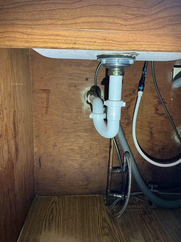 Replaced deteriorated drain assembly with new PVC components, installing proper S-trap configuration through floor joists and connecting to existing drain line. Installed new P-trap under kitchen sink with appropriate connections to sink drain flange, ensuring proper drainage and eliminating previous water staining issues.