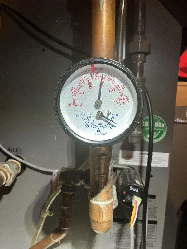 Inspected 10-year-old boiler in basement exhibiting water leakage from the bottom. Observed pressure reading of approximately 40-45 PSI on the system gauge, with signs of aging connections and minor corrosion at valve fittings. Identified and replaced faulty T-shaped brass valve connection where copper piping meets the boiler outlet, resolving the leak issue.
