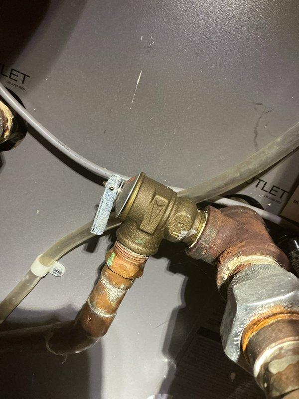 Inspected 10-year-old boiler in basement exhibiting water leakage from the bottom. Observed pressure reading of approximately 40-45 PSI on the system gauge, with signs of aging connections and minor corrosion at valve fittings. Identified and replaced faulty T-shaped brass valve connection where copper piping meets the boiler outlet, resolving the leak issue.