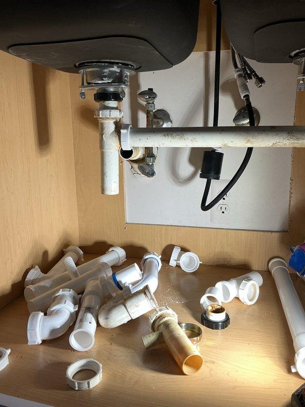 Performed diagnostic assessment of kitchen sink plumbing system requiring complete assembly. Examined disconnected PVC components and existing metal drain assembly with P-trap configuration. Determined requirements for proper installation of sink drain, P-trap connection, and potential dishwasher hookup. Documented current state with photos showing partially installed components and provided detailed estimate for completing the plumbing installation.