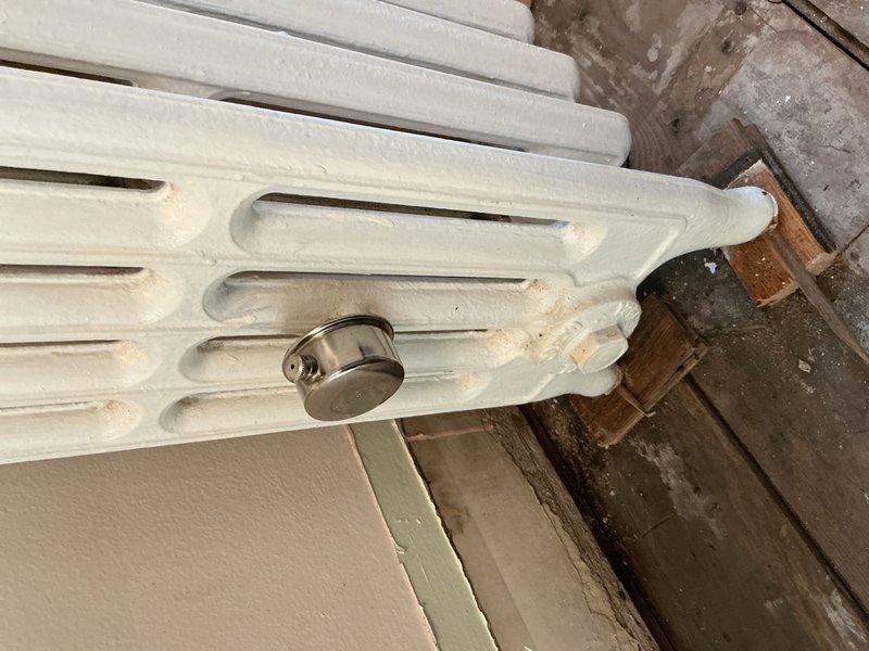 Inspected white cast iron radiator system connected to basement boiler that customer reported was leaking. Identified aging valve assembly with visible corrosion as the source of water leakage. Recommended replacement of the radiator valve and scheduling a comprehensive boiler system evaluation due to the unit's advanced age and potential for additional component failures.