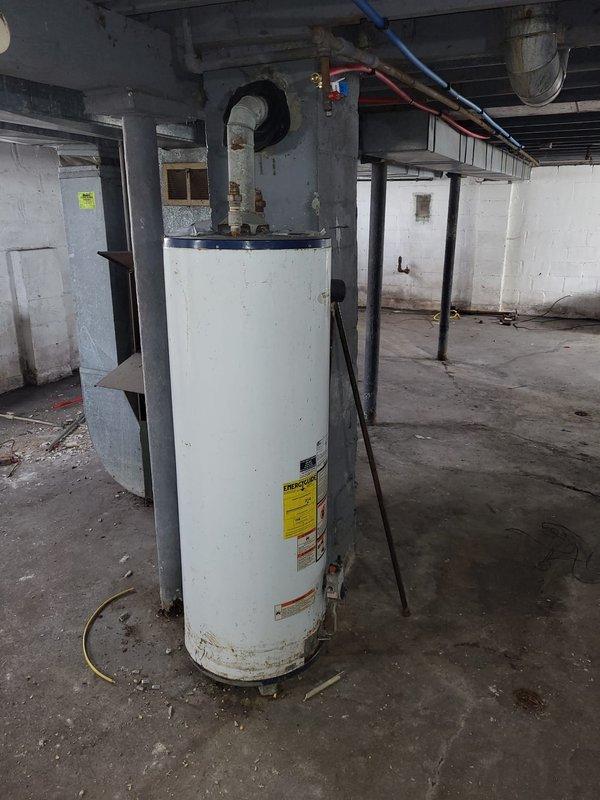 Conducted a full system estimate for furnace replacement in a residential basement. Inspection revealed an aging HVAC system with a green cabinet furnace showing significant wear alongside a cylindrical water heater with visible corrosion at its base. Observed deteriorating ductwork, moisture damage on ceiling surfaces, and recommended complete system replacement due to age and condition of equipment.