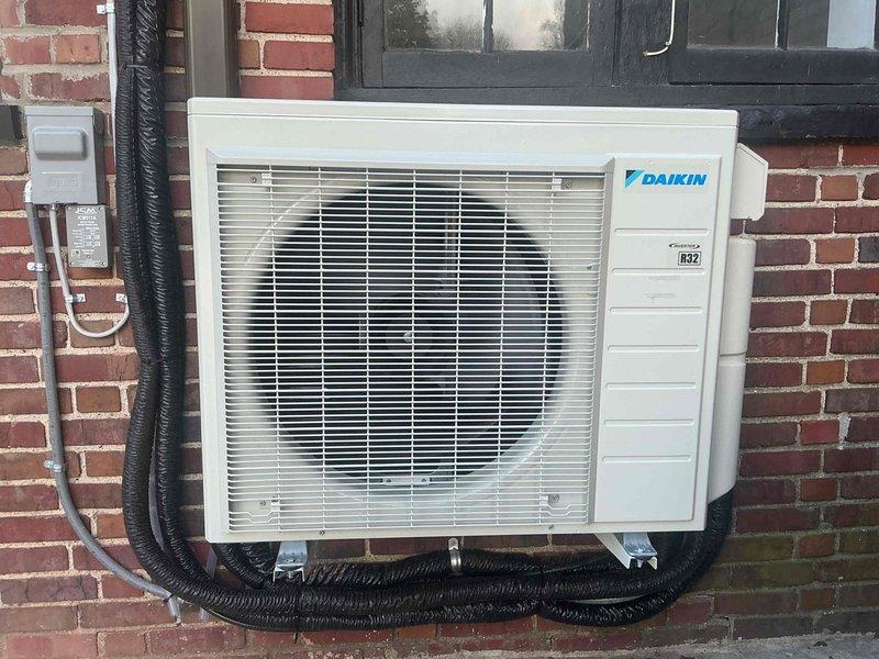 Responded to callback for Daikin mini-split system showing "High Discharge Pipe Control" error message. Inspected outdoor unit mounted on brick wall with proper insulated refrigerant lines and electrical connections. System was diagnosed, error cleared, and unit returned to normal operation with verification of proper discharge temperatures.