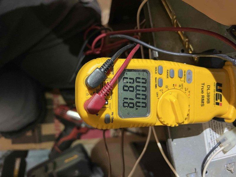 Performed comprehensive tune-up on 21-year-old HVAC system located in basement. Inspected and documented condition of metal mesh filter showing some discoloration and accumulation of debris. Conducted electrical diagnostics using UEi DL389B multimeter, measuring voltage readings of 83.1V and 81.0V. Completed standard inspection of humidifier, thermostat, and hot water tank as part of maintenance service.