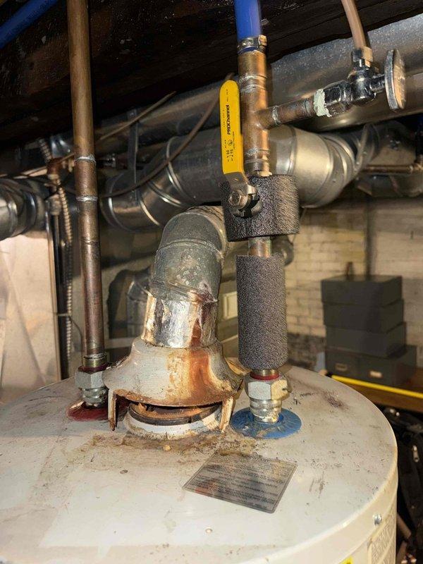 Responded to service call for a non-operational furnace with reported water damage. Upon inspection, found evidence of water infiltration affecting electrical components, with multimeter testing confirming damage to wiring connections. Observed significant corrosion on furnace connections and nearby water heater plumbing, with aging components showing considerable wear on the 15+ year old system.