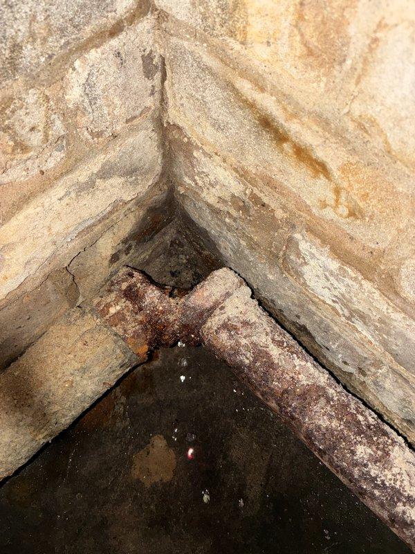 Responded to service call for a 10+ year old steam boiler system with broken steam radiator pipe causing water leakage throughout radiators. Diagnostic inspection revealed significant water damage in basement, with standing water on concrete floor and extensive corrosion on horizontal piping. Observed considerable moisture deterioration and mineral deposits on foundation walls near the affected area.