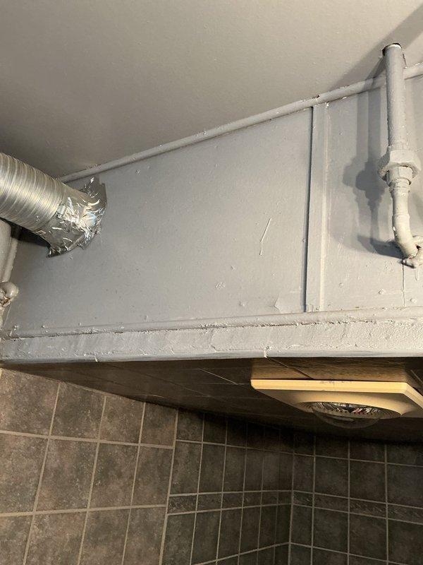 Completed inspection and repair of exposed plumbing infrastructure in bathroom area, including vertical PVC pipe installation with proper fittings and ventilation system connection. Addressed corner floor-to-wall junction where metal supply line emerges from hexagonal tile flooring, ensuring proper sealing and alignment with existing plumbing components.