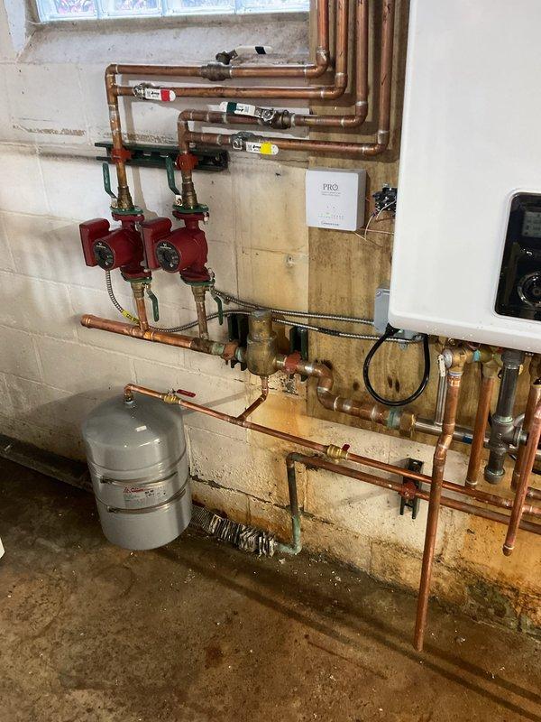 Conducted follow-up inspection on Navien boiler system after previous repairs due to customer's report of inefficient heating. Examined complete hydronic system including circulation pumps, expansion tank, and copper supply/return lines. System appears professionally installed with proper valves and gauges in place. No visible issues identified with the equipment or installation that would cause heating inefficiency.