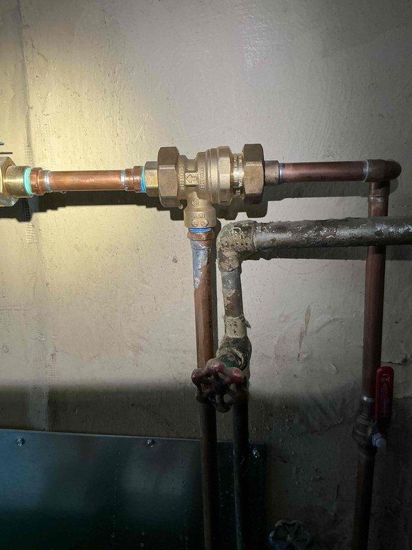 Diagnosed water leak originating from 12-year-old boiler located in kitchen. Identified heavily corroded pipe section with significant mineral deposits as the source of leakage. Replaced deteriorated section with new brass backflow preventer valve and copper pipe connections, ensuring proper seals at junction points to prevent future leakage.