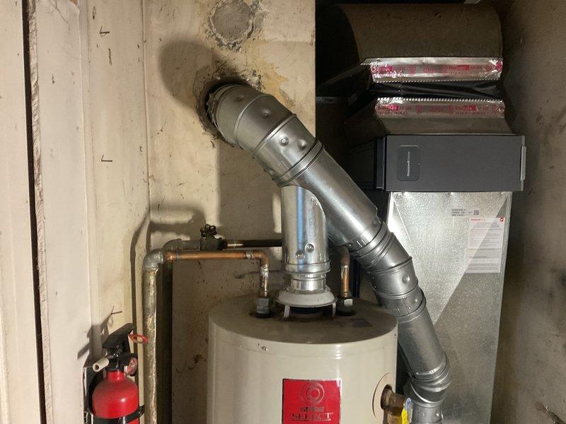 Responded to service call for leaking water heater in residential kitchen. Inspected tank-type water heater with metal exhaust venting and surrounding connections. Identified and repaired leak source, ensuring proper operation and verifying no further moisture issues around the unit mounted on wooden platform.