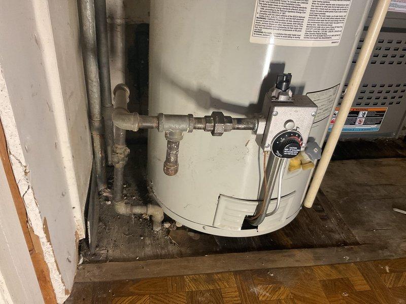 Responded to service call for leaking water heater in residential kitchen. Inspected tank-type water heater with metal exhaust venting and surrounding connections. Identified and repaired leak source, ensuring proper operation and verifying no further moisture issues around the unit mounted on wooden platform.