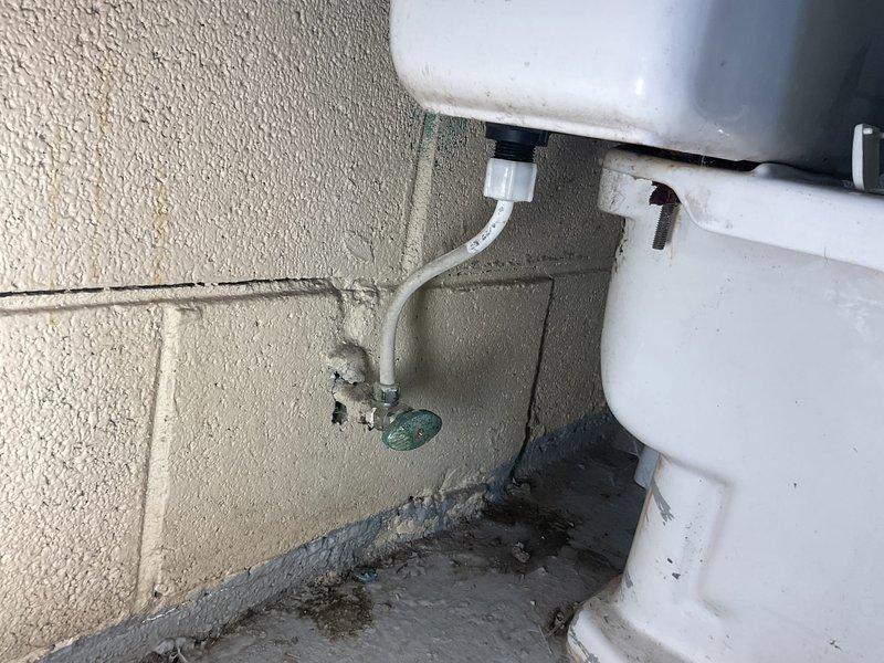 Responded to service call for a leaky water supply line at commercial toilet installation. Upon inspection, found corroded copper shut-off valve with visible water damage to surrounding concrete and significant mineral/rust buildup in tank with discolored water. Replaced damaged supply line and shut-off valve to resolve leak, then flushed system to remove sediment and restore proper function.