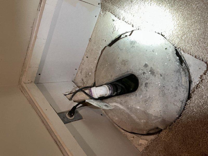 Performed an assessment for a battery backup sump pump installation. Inspected existing ceiling damage and plumbing infrastructure, noting significant water damage and an exposed electrical fixture through a ceiling opening. Examined the current sump system connection point with PVC piping and valve assembly to determine appropriate backup system specifications.