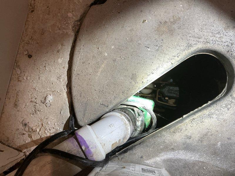 Performed an assessment for a battery backup sump pump installation. Inspected existing ceiling damage and plumbing infrastructure, noting significant water damage and an exposed electrical fixture through a ceiling opening. Examined the current sump system connection point with PVC piping and valve assembly to determine appropriate backup system specifications.