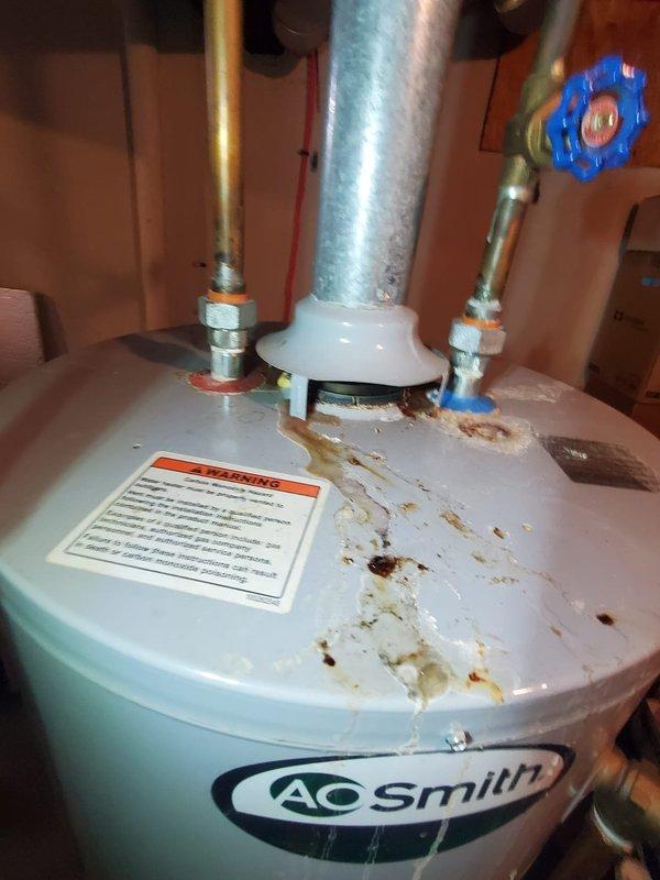 Performed diagnostic assessment on furnace and water heater systems following water submersion in basement. Observed significant corrosion and mineral deposits on A.O. Smith water heater unit, particularly around top connections and tank surface. Documented damage with photos showing compromised equipment condition and surrounding utility area for comprehensive damage evaluation.