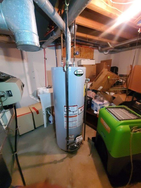 Performed diagnostic assessment on furnace and water heater systems following water submersion in basement. Observed significant corrosion and mineral deposits on A.O. Smith water heater unit, particularly around top connections and tank surface. Documented damage with photos showing compromised equipment condition and surrounding utility area for comprehensive damage evaluation.