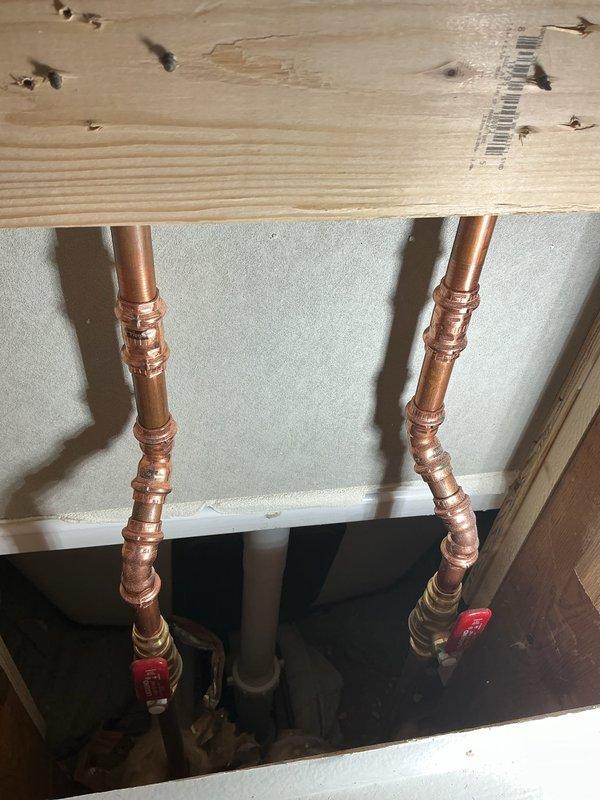 Conducted inspection of plumbing code violations in two bathrooms. Identified improper utility box installation with exposed braided supply line and drainage hose in a narrow wall cavity. Also found copper supply lines with multiple fittings and red valve handles mounted to wooden support beams, requiring proper securing and code-compliant installation.