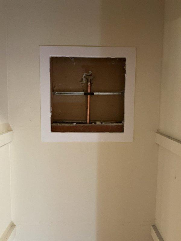 Accessed plumbing system through wall access panel to inspect copper supply line and mounting bracket. Performed maintenance on bathtub/shower fixture with blue tile surround, ensuring proper function of chrome faucet, controls, and drain.