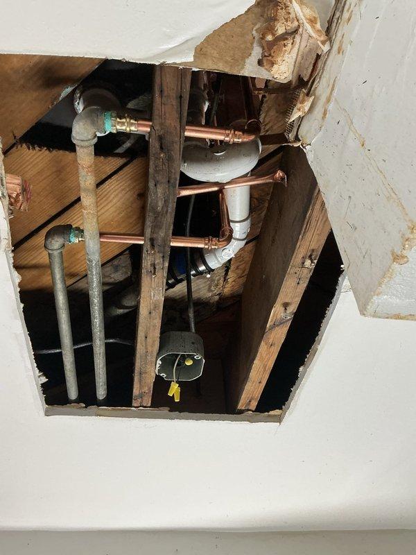Accessed and repaired Ken waste and overflow system by opening wall cavity to expose damaged plumbing infrastructure. Replaced deteriorated copper pipes and connections in bathroom, addressing water damage on wooden supports and restoring proper drainage function through the installation of new fittings.