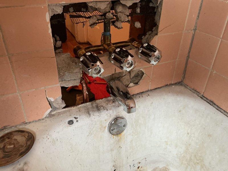 Accessed and repaired Ken waste and overflow system by opening wall cavity to expose damaged plumbing infrastructure. Replaced deteriorated copper pipes and connections in bathroom, addressing water damage on wooden supports and restoring proper drainage function through the installation of new fittings.