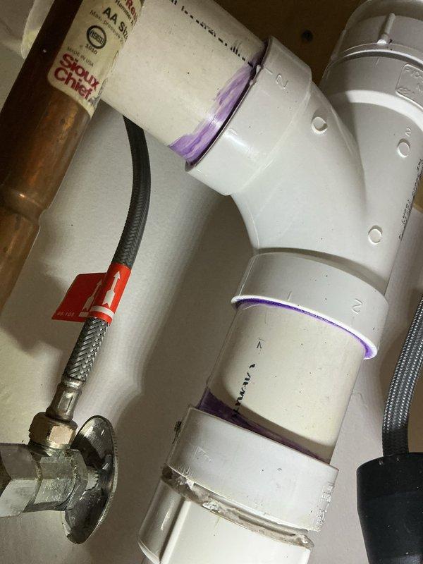 Performed camera inspection of PVC plumbing system, identifying deterioration at wall connection point with visible debris and staining. Documented condition of multiple pipe joints, including PVC with purple primer markings and metal-braided supply lines connected to copper components. Recommended and sold necessary repair services to address the identified issues.