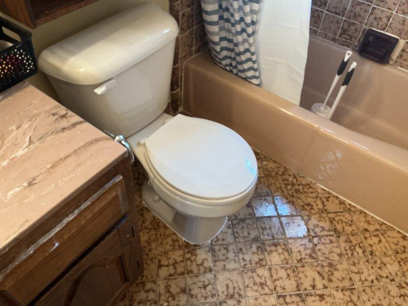 Responded to service call regarding a wobbly toilet in upstairs bathroom. Upon inspection, identified deteriorated toilet flange as the source of instability. Documented condition of bathroom fixtures and surrounding floor area, noting significant corrosion and buildup around a separate floor drain that may require future attention. Diagnostic completed; awaiting landlord approval for repair work.
