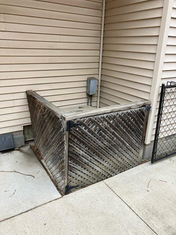 Conducted assessment of a 30-year-old air conditioning system that is currently operational. Inspected exterior condenser unit housed within weathered wooden lattice enclosure on concrete pad showing minor cracking. Examined electrical connections including junction box and conduit. Customer is considering replacement options for this aging but functional system.