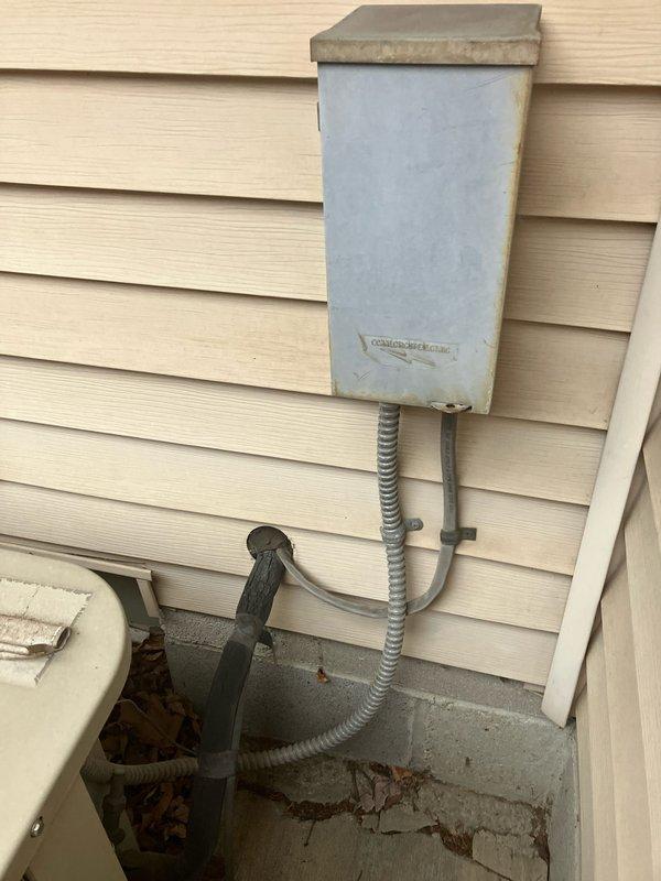 Conducted assessment of a 30-year-old air conditioning system that is currently operational. Inspected exterior condenser unit housed within weathered wooden lattice enclosure on concrete pad showing minor cracking. Examined electrical connections including junction box and conduit. Customer is considering replacement options for this aging but functional system.