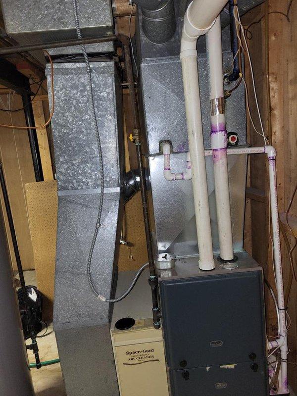 Conducted a comprehensive assessment of the aging heating system located in the basement, documenting the current installation which includes a furnace unit with connected PVC ventilation pipes, metal ductwork, and integrated Space-Gard air filtration system. Prepared replacement quote for complete HVAC system upgrade, noting proximity to water heater and existing utility infrastructure that will need to be considered during installation.
