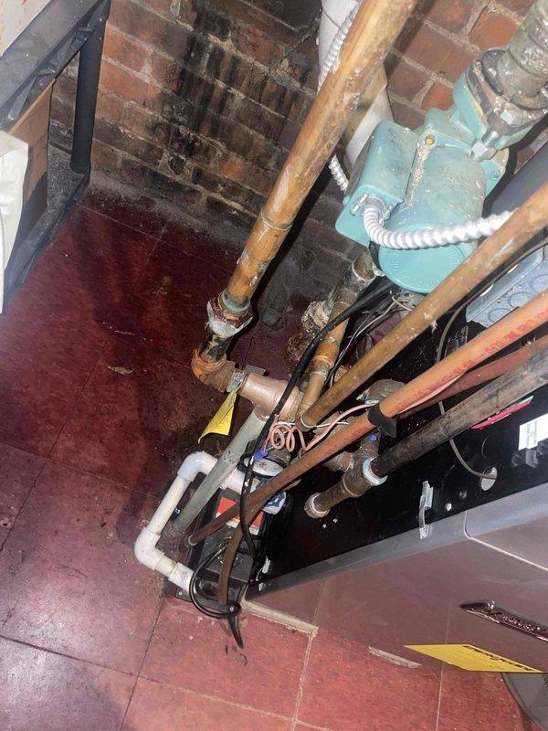 Conducted assessment of aging hot water boiler system in residential basement showing multiple pipe leaks at joints and improper exhaust configuration (mixed PVC and metal components). Documented significant concerns including vibration during operation, signs of water damage on surrounding brick walls, and visible corrosion on copper piping components. Estimate provided for necessary repairs to seal leaking connections and standardize exhaust system to prevent potential safety hazards.