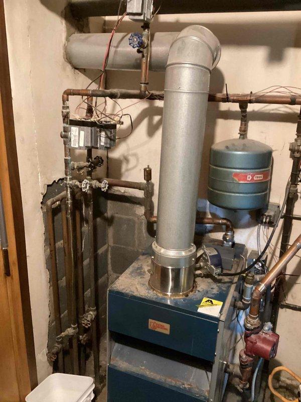 Responded to service call for a leaking boiler over 10 years old located in the basement. Upon inspection, identified water staining on the ceiling near the exhaust flue, indicating ongoing leakage from the aging system. Performed diagnostic assessment of the complete heating system including the boiler unit, expansion tank, and associated copper piping network to determine the source of the leak.