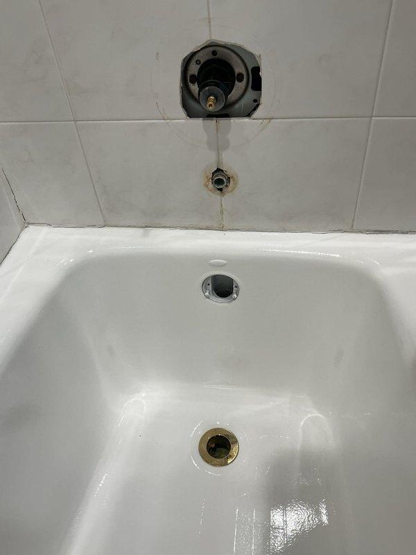 Performed inspection and assessment of shower fixture installation requirements in first floor bathroom of a 75-year-old residence. Examined existing plumbing infrastructure via access panel, revealing aged copper supply lines and supporting framework. Evaluated bathtub area which showed partially installed shower valve with visible water damage around plumbing openings in tile wall. Documentation completed with detailed photographs for comprehensive project planning.