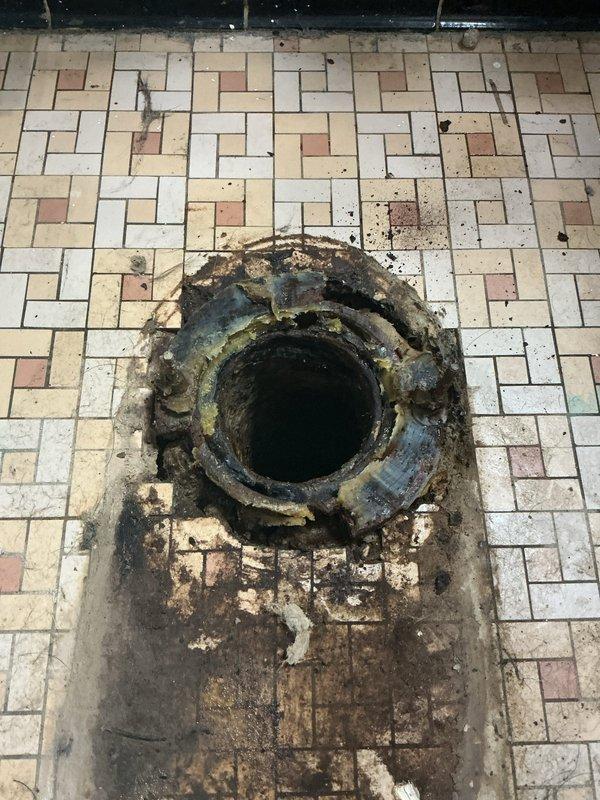 Inspected bathroom toilet with significant internal tank deterioration and mineral buildup, requiring flush valve replacement and thorough cleaning of components. Also addressed severely corroded floor drain with extensive surrounding water damage, replacing the drain assembly and sealing to prevent further deterioration of the tile flooring.