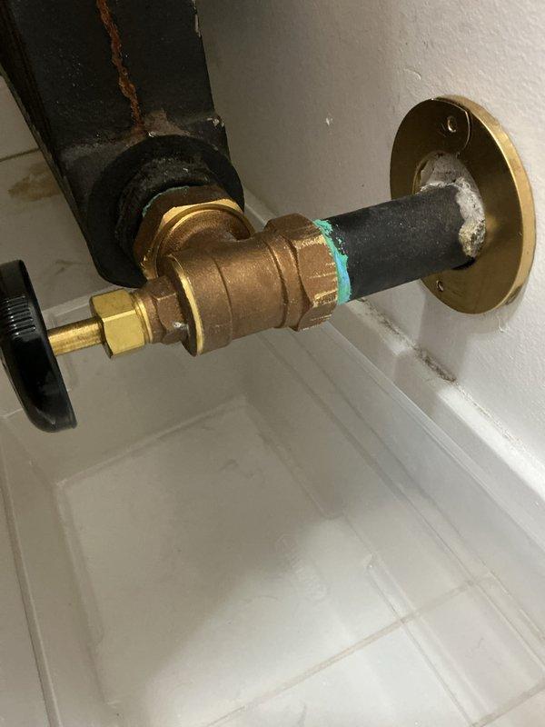 # Service Report

Responded to service call for leaking radiator valve on newly installed boiler system (5 months old). Located equipment in upstairs second-floor bathroom. Upon inspection, identified persistent leak at radiator supply valve connection point. Examined brass valve assembly with compression fittings and noted compromised seal at connection interface. Inspected black insulated supply pipe, wall flange mounting, and associated plumbing components installed over drain pan. Documented valve assembly configuration showing brass body, compression fittings, and connection points for warranty and quality assurance purposes. Issue identified as installation-related defect requiring senior technician expertise to properly diagnose and resolve recurring failure on new equipment. Photographs captured of valve assembly, compression fittings, pipe connections, and drain pan arrangement for technical review and corrective action planning.