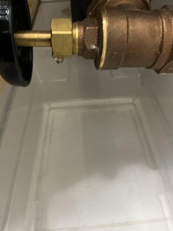 # Service Report

Responded to service call for leaking radiator valve on newly installed boiler system (5 months old). Located equipment in upstairs second-floor bathroom. Upon inspection, identified persistent leak at radiator supply valve connection point. Examined brass valve assembly with compression fittings and noted compromised seal at connection interface. Inspected black insulated supply pipe, wall flange mounting, and associated plumbing components installed over drain pan. Documented valve assembly configuration showing brass body, compression fittings, and connection points for warranty and quality assurance purposes. Issue identified as installation-related defect requiring senior technician expertise to properly diagnose and resolve recurring failure on new equipment. Photographs captured of valve assembly, compression fittings, pipe connections, and drain pan arrangement for technical review and corrective action planning.