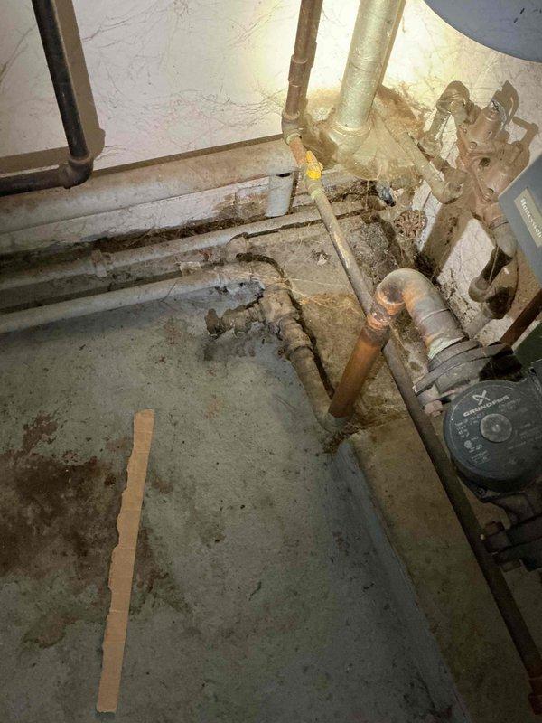 # Job Description

Responded to service call for 20-year-old residential boiler system requiring backflow preventer installation and boiler draining service. Upon arrival, inspected existing hydronic heating system located in basement utility area. System consisted of older green boiler unit with associated circulation pump and copper piping distribution network showing significant age-related patina and oxidation.

Performed complete boiler drain-down procedure to facilitate backflow preventer installation and system maintenance. Shut down boiler and allowed adequate cooling time. Isolated system and drained water from boiler and associated piping through existing drain valves. Inspected circulation pump during drain-down process and confirmed operational condition despite visible age-related wear on exterior housing.

Installed code-compliant backflow preventer on water supply line to boiler system per local plumbing requirements. Made necessary connections to existing copper supply 