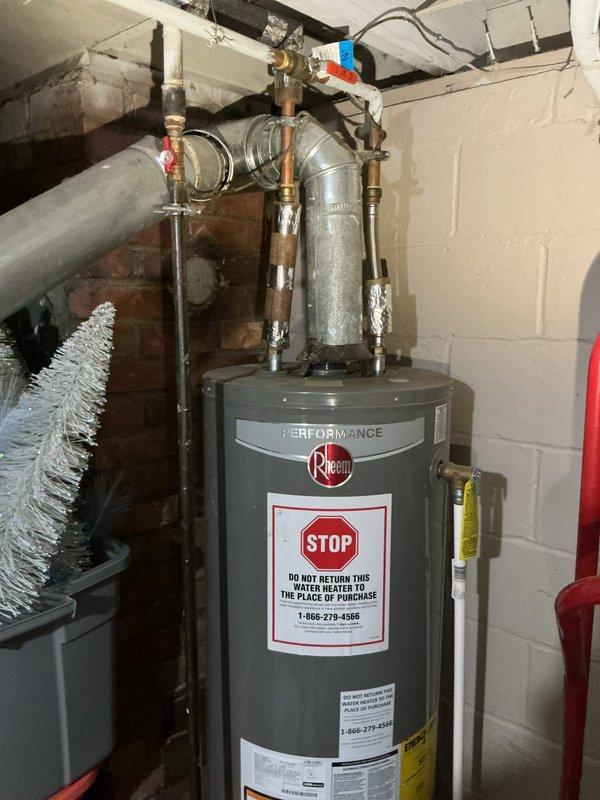 # Plumbing Service Report - Water Heater Replacement

Responded to service call for leaking water heater in basement. Upon arrival, confirmed active leak originating from tank area. Performed visual inspection of existing unit and surrounding plumbing connections to identify source of failure.

Shut off water supply and drained existing water heater to prevent further water damage. Disconnected inlet and outlet copper piping, temperature and pressure relief valve discharge line, and gas supply connection. Removed failed unit from service location.

Installed new Rheem Performance tankless water heater as replacement. Positioned unit against concrete block wall in same location as previous heater. Connected cold water inlet and hot water outlet lines using existing copper piping infrastructure. Installed new temperature and pressure relief valve with proper discharge piping. Reconnected gas supply line with appropriate fittings and verified connections for safety.

Mounted expansion tan