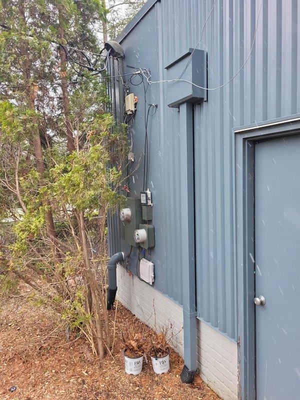 # Electrical Estimate - Generator Installation

Conducted comprehensive site assessment for new whole home generator installation at residential property with corrugated metal siding and existing electrical service infrastructure. Evaluated current electrical service configuration including meter base, service entrance conductors, and overhead utility connection points to determine optimal generator placement and integration requirements.

Documented existing electrical infrastructure consisting of dual meter housings, exterior-mounted disconnect equipment, and conduit routing along building exterior. Assessed available space on side wall adjacent to service entrance for generator pad placement and transfer switch installation. Identified clear access pathway for fuel line connection and verified adequate clearance from building openings per manufacturer specifications and local code requirements.

Analyzed electrical service capacity and load requirements to properly size automatic tr